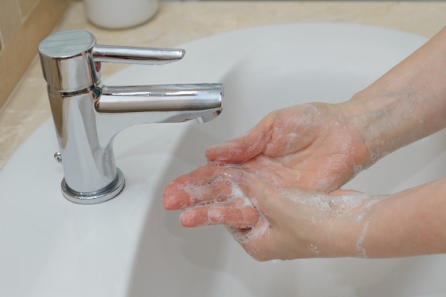 Vista delle mani femminili in schiuma saponosa sotto il primo piano dell'acqua di rubinetto