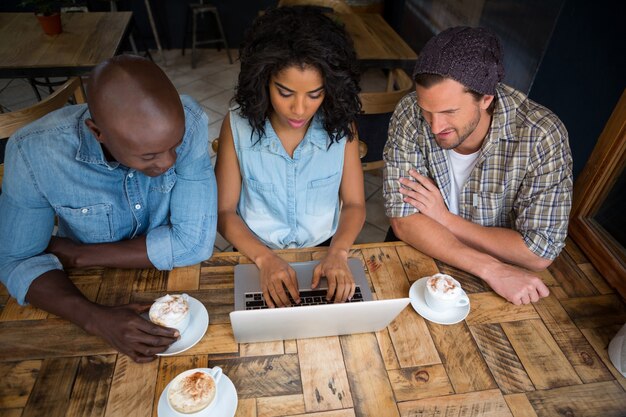 Vista di alto angolo di amici che utilizzano computer portatile al tavolo di legno nella caffetteria