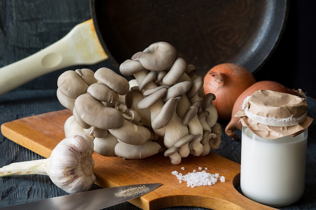 Vista di funghi ostrica fresca con panna, spezie, erbe aromatiche e verdure su fondo di legno scuro.