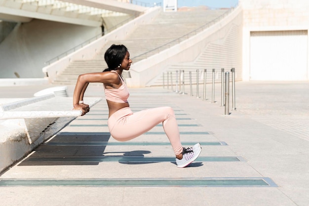 Vista di profilo dell'atleta femminile afroamericano che fa esercizio del tricipite sul concetto di formazione di allenamento di allenamento di allenamento di sport di forma fisica della panca della città