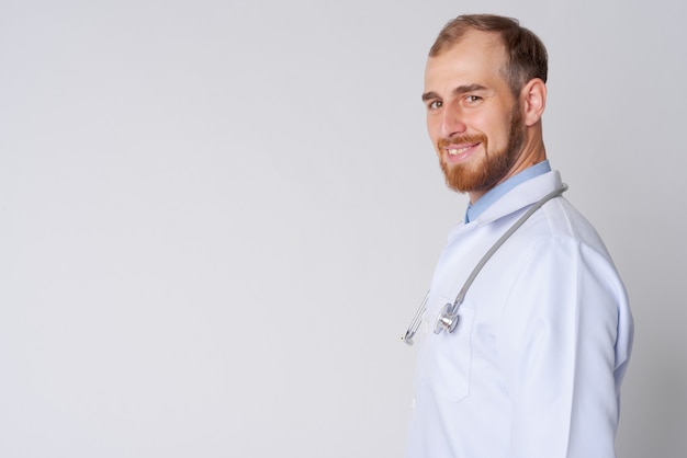 Vista di profilo di felice giovane barbuto medico che guarda l'obbiettivo