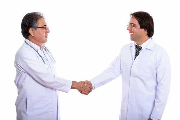 Vista di profilo di felice giovane e senior uomo persiano medico sorridente e handshake