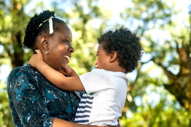 Vista di profilo di una madre africana felice che abbraccia il suo bambino in natura