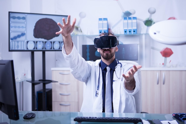 Vista di un medico di sesso maschile in possesso di un rendering 3d utilizzando l'auricolare per realtà virtuale. Dottore nel suo ufficio che lavora.