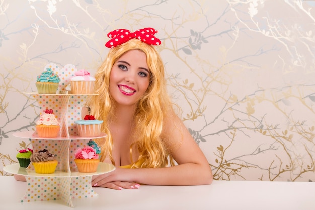 Vista di una bella ragazza bionda pinup con cupcakes colorati su un tavolo.