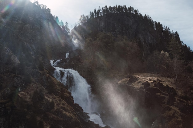 Vista di una cascata dalla montagna con una foresta alla luce del sole