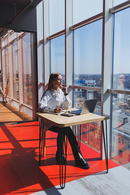 Vista di una donna concentrata in abbigliamento casual che digita sul netbook mentre lavora a un nuovo progetto seduto a tavola in uno spazio di lavoro moderno