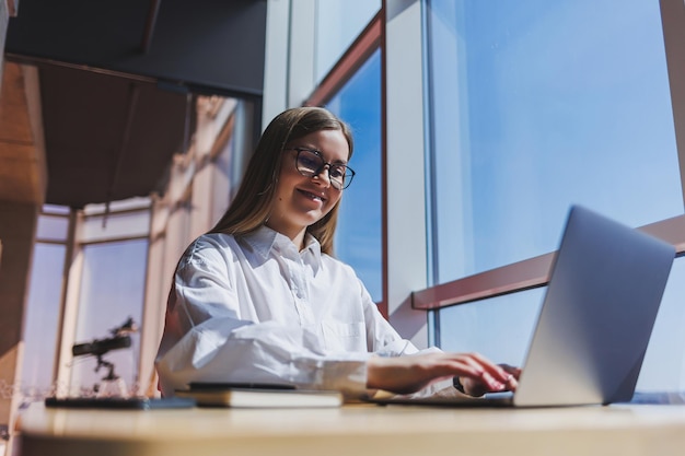 Vista di una donna concentrata in abbigliamento casual che digita sul netbook mentre lavora a un nuovo progetto seduto a tavola in uno spazio di lavoro moderno