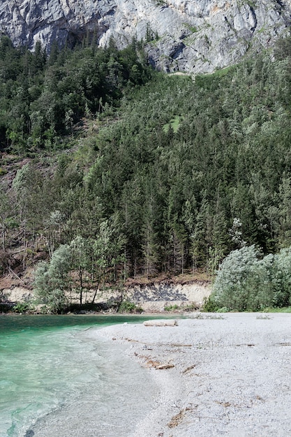 Vista di una spiaggia selvaggia con lago di montagna di ciottoli bianchi con colore turchese di acqua, scogliere e foreste. Il concetto di natura, montagne, pista, viaggi.