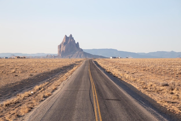 Vista di una strada in un deserto secco con una cima di montagna Shiprock sullo sfondo