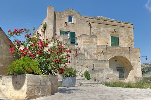 Vista di una vecchia casa a Matera nei sassi con piante fiorite sotto il cielo blu