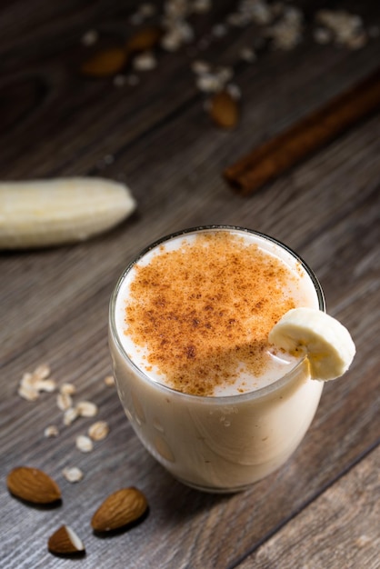 Vista diagonale di frullato di banana con cacao e bastoncini di cannella su uno sfondo di legno