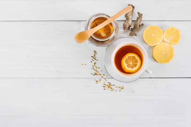Vista elevata del tè al limone; miele e zenzero sullo sfondo in legno
