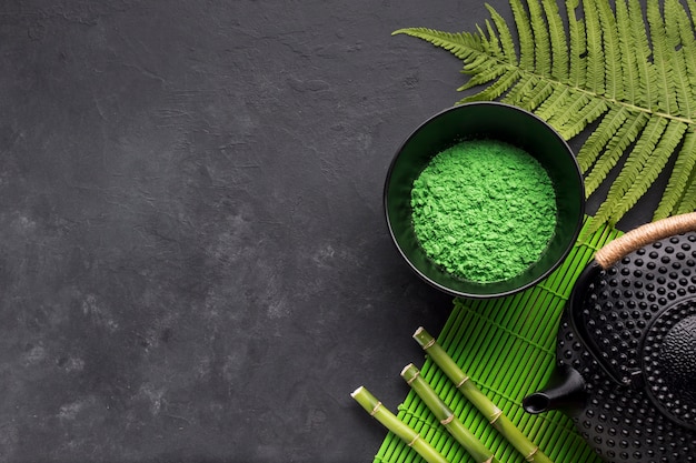 Vista elevata della polvere verde del tè di matcha con le foglie della felce e il bastone di bambù su superficie nera