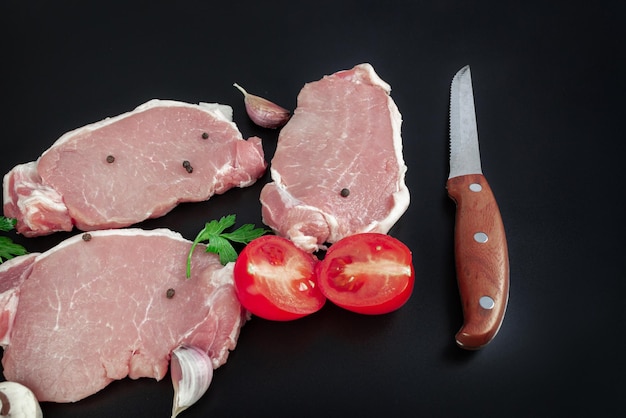 Vista elevata di bistecche di carne cruda e spezie in cucina con coltello da carne su sfondo scuro