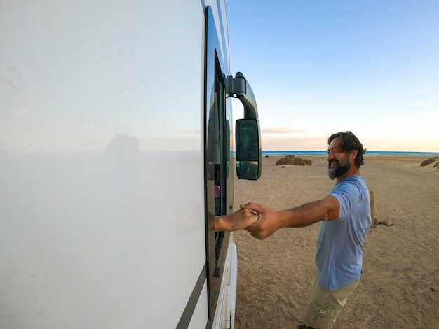 Vista esterna della coppia che si tiene per mano Donna all'interno di un camper e uomo all'esterno sorridente Viaggio per vacanze vacanza concetto di stile di vita spiaggia e oceano sullo sfondo