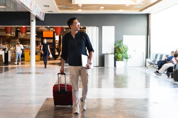Vista frontale bell'uomo ispanico con valigia trolley che cammina all'aeroporto Concetto di viaggio