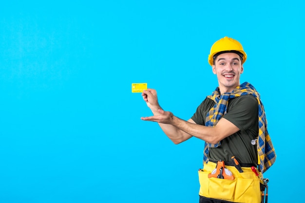Vista frontale costruttore maschio in casco giallo in possesso di carta di credito su sfondo blu architettura lavoratore edile costruttore colore piatto