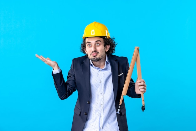 vista frontale costruttore maschio nel casco che tiene il dispositivo in legno sullo sfondo blu lavoro costruttore aziendale architettura lavori edili design
