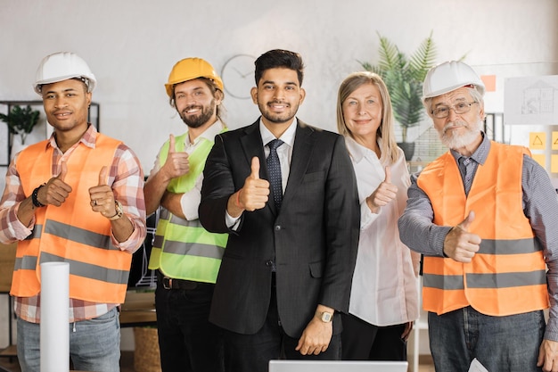 Vista frontale degli architetti dei costruttori che guardano la macchina fotografica mentre si trovano in un ufficio moderno e leggero