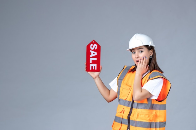 Vista frontale del costruttore femminile che tiene il bordo rosso di vendita sulla parete bianca