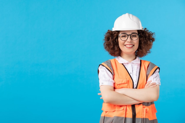 Vista frontale del costruttore femminile felice in uniforme sulla parete blu