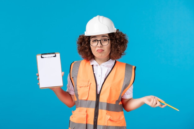 Vista frontale del costruttore femminile in uniforme con piccola nota sulla parete blu