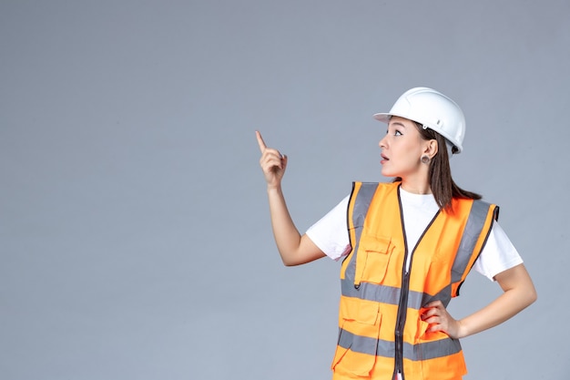 Vista frontale del costruttore femminile in uniforme sul muro grigio