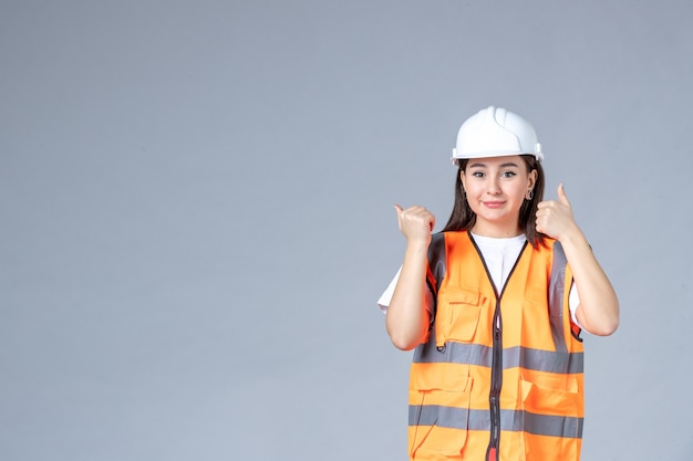 Vista frontale del costruttore femminile in uniforme sul muro grigio