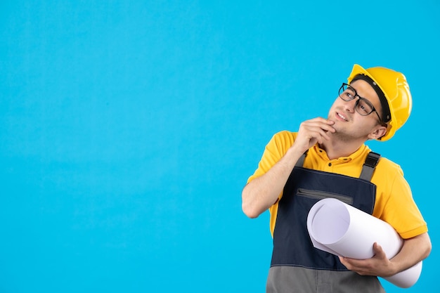 Vista frontale del costruttore maschio di pensiero in uniforme con il piano di carta sull'azzurro