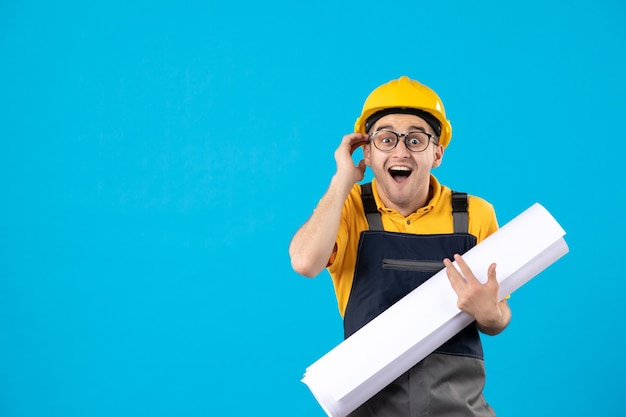 Vista frontale del costruttore maschio in uniforme gialla e casco con piano sulla parete blu