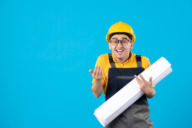 Vista frontale del costruttore maschio in uniforme gialla e casco con piano sulla parete blu