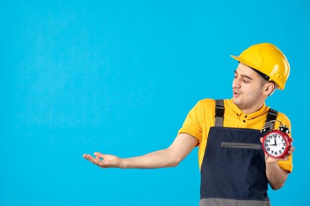 Vista frontale del lavoratore maschio in uniforme gialla con orologi sull'azzurro