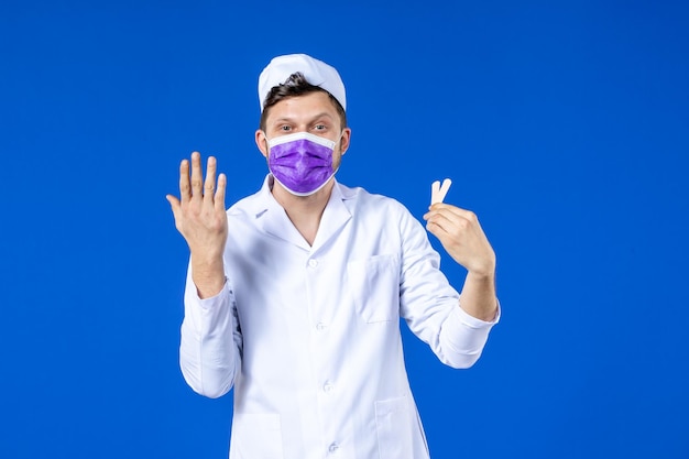 Vista frontale del medico maschio in tuta medica e maschera che tiene piccoli cerotti medici sull'azzurro