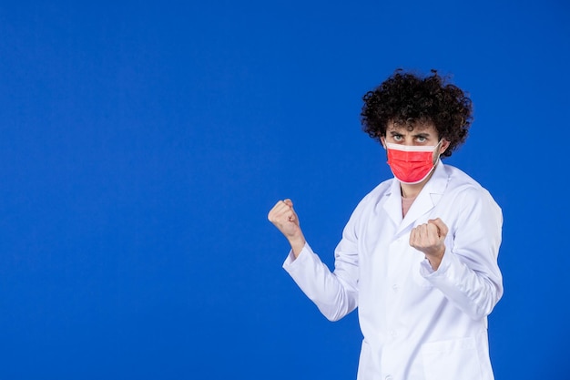 Vista frontale del medico maschio in tuta medica e maschera su superficie blu