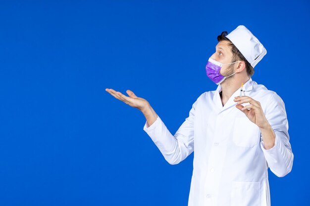 Vista frontale del medico maschio in tuta medica e maschera tenendo l'iniezione sull'azzurro