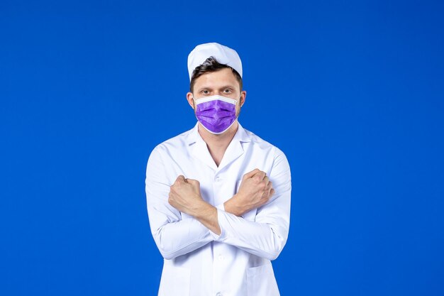 Vista frontale del medico maschio in tuta medica e maschera viola sull'azzurro