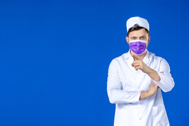 Vista frontale del medico maschio in tuta medica e maschera viola sull'azzurro