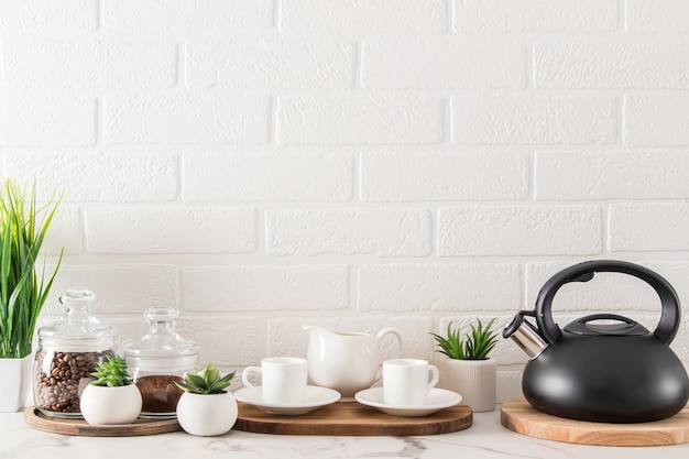 Vista frontale del piano di lavoro della cucina moderna nei toni del bianco con tazze da caffè, bollitore, lattine di caffè il concetto di una cucina piacevole