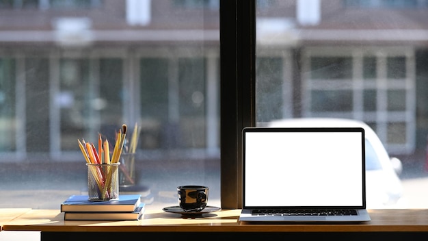 Vista frontale del posto di lavoro alla moda con il computer portatile, la tazza di caffè, i libri e la cancelleria sulla tavola di legno.