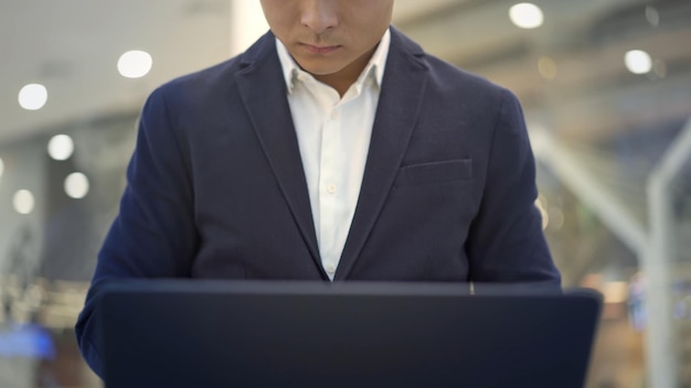 Vista frontale dell'uomo d'affari maschio asiatico in vestito che lavora con il computer portatile sulle ginocchia