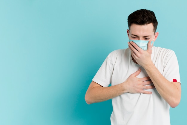 Vista frontale dell'uomo malato che tossisce mentre indossa una maschera medica