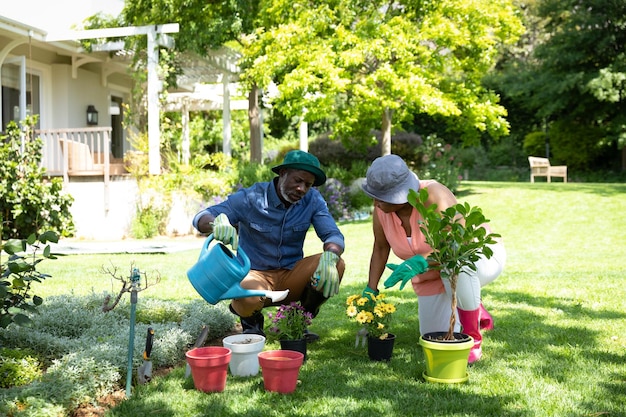 Vista frontale della coppia afroamericana senior in giardino, giardinaggio e piante d'innaffiatura. Famiglia che si gode il tempo a casa, concetto di stile di vita