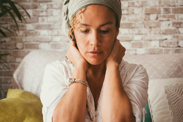 Vista frontale della donna che si tocca il collo e guarda in basso con il divano e l'interno della casa sullo sfondo Concetto di stato mentale e stile di vita Attraenti donne di mezza età Ansia burnout mentale