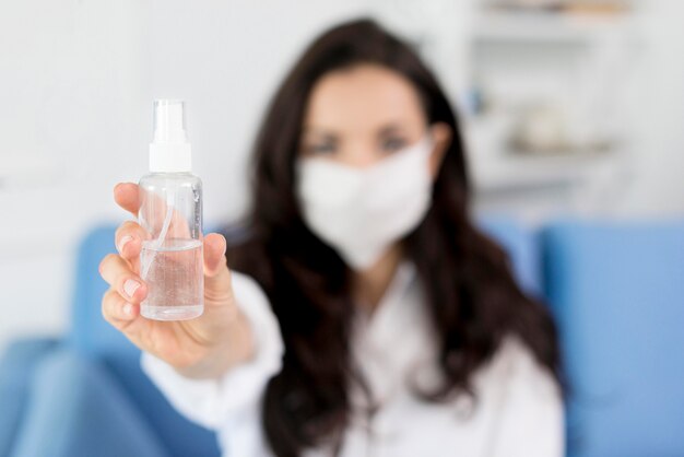 Vista frontale della donna defocused con disinfettante per le mani della tenuta della maschera di protezione