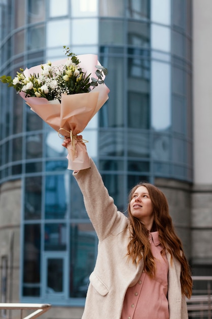 Vista frontale della donna felice che tiene il mazzo di fiori all'esterno