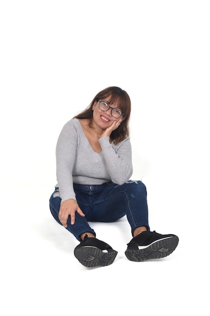Vista frontale della donna felice seduta sul pavimento mano sul viso su sfondo bianco