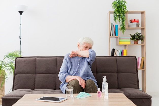 Vista frontale della donna più anziana a casa che tossisce nel gomito