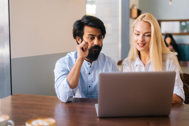 Vista frontale della giovane imprenditrice e uomo d'affari concentrati che lavorano insieme utilizzando il laptop seduto al bar clsoeup