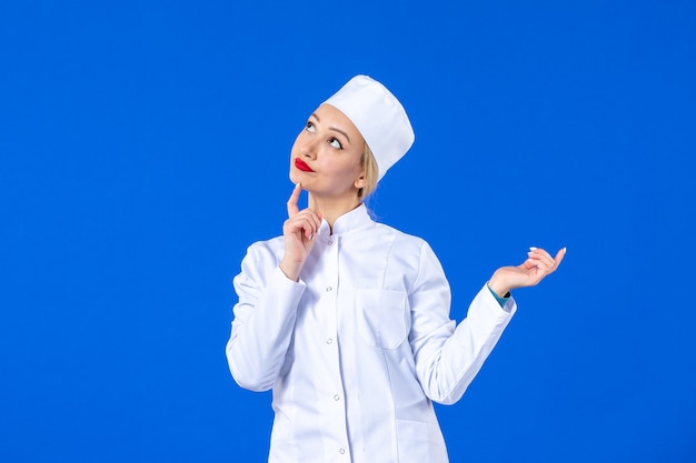 vista frontale della giovane infermiera in tuta medica sulla parete blu